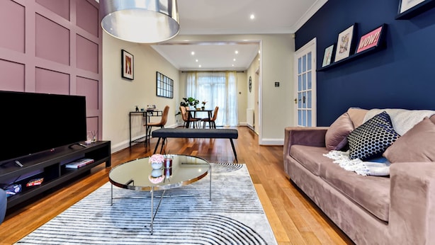A modern living room with a flat-screen TV, a glass coffee table, a sofa, and a dining area with chairs and a table. - Luxurious Pad in an Unbeatable Wembley Location (Wembley)