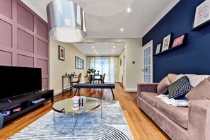 A modern living room with a flat-screen TV, a glass coffee table, a sofa, and a dining area with chairs and a table. - Luxurious Pad in an Unbeatable Wembley Location (Wembley)