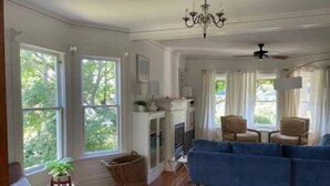 A spacious living room with a blue sofa, a fireplace, and large windows offering a view of greenery. - La Stella - An Oasis in the City for large groups (Seattle)