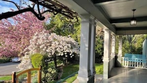 A covered porch with white columns, a wooden railing, and a view of cherry blossoms. - La Stella - An Oasis in the City for large groups (Seattle)