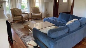 A living room with a blue sofa, two armchairs, a coffee table, a lamp, and a television. - La Stella - An Oasis in the City for large groups (Seattle)