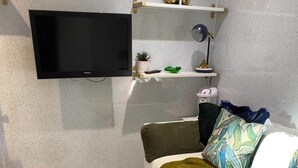 Une chambre à coucher avec un lit, un téléviseur fixé au mur, une petite étagère avec des objets décoratifs et un tapis vert.