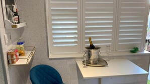 Une cuisine avec une chaise bleue, un plan de travail blanc et une fenêtre avec des stores.
