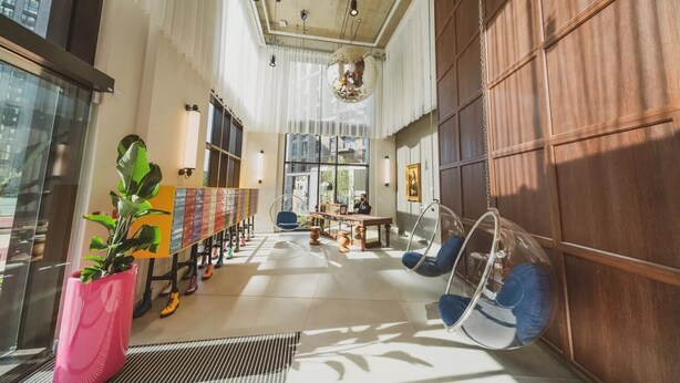 A spacious lobby with a long reception desk, clear glass chairs, and a large potted plant. - The Robinson (Wembley)