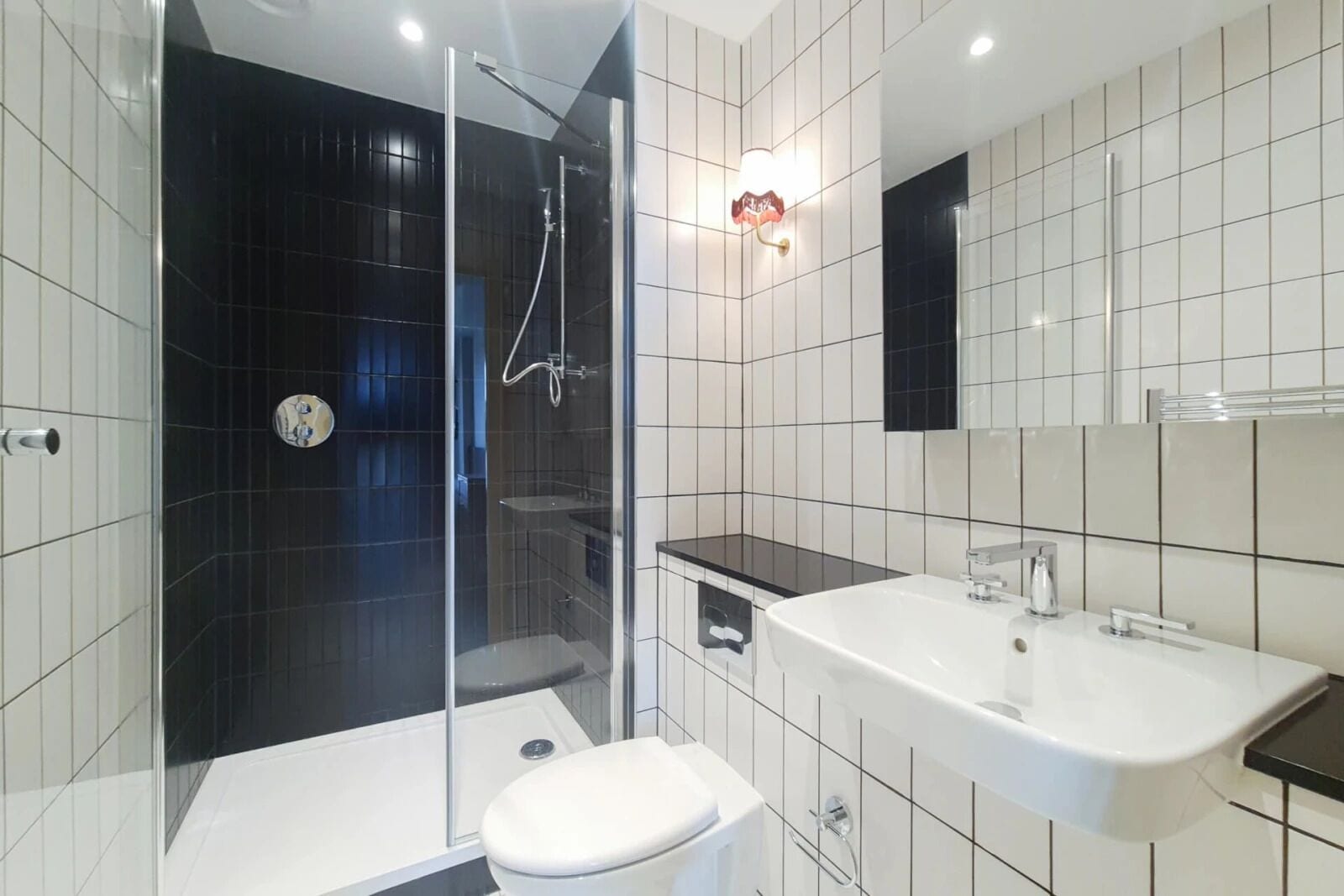 A modern bathroom with a glass-enclosed shower, a white toilet, a sink, and a mirror.