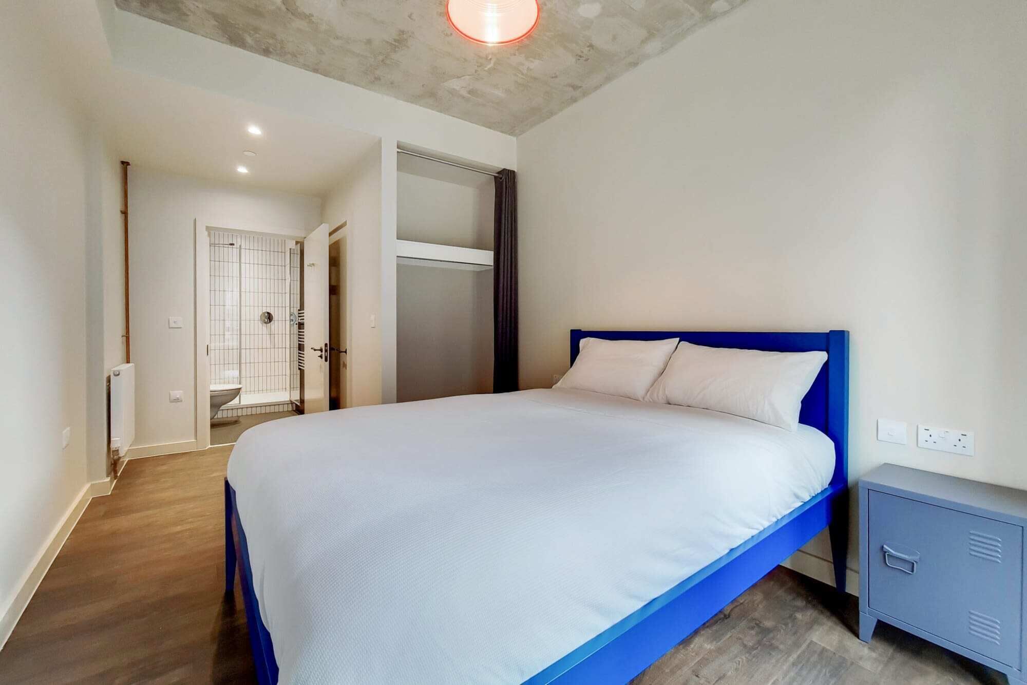 Ein Schlafzimmer mit Bett, Nachttisch, Kleiderschrank, Dusche und einer Tür zu einem anderen Raum.