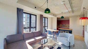 A modern living room with a sofa, chairs, a glass table, and a kitchen in the background.
