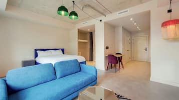 A modern hotel room with a bed, blue sofa, and a dining area with a table and chairs.