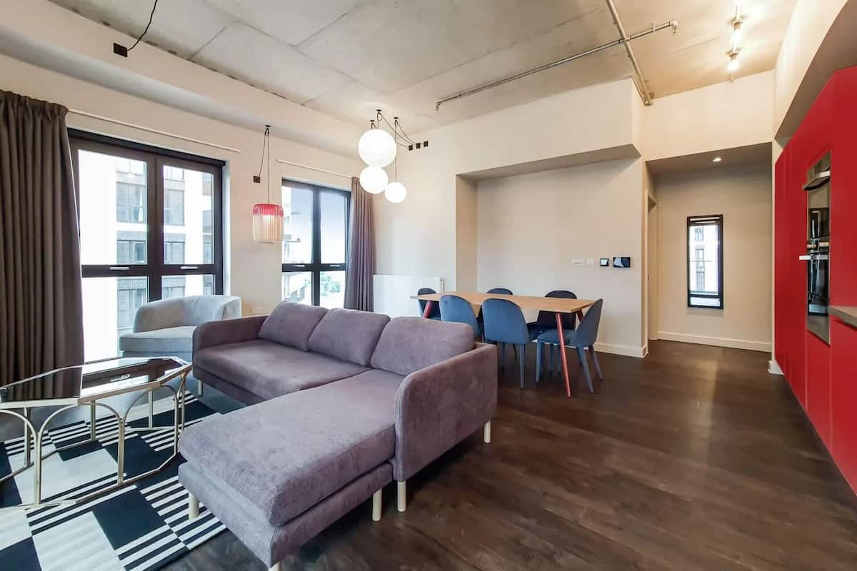 Uma sala de estar moderna com sofá, mesa de jantar, cadeiras e uma área de cozinha com uma parede de destaque vermelha.