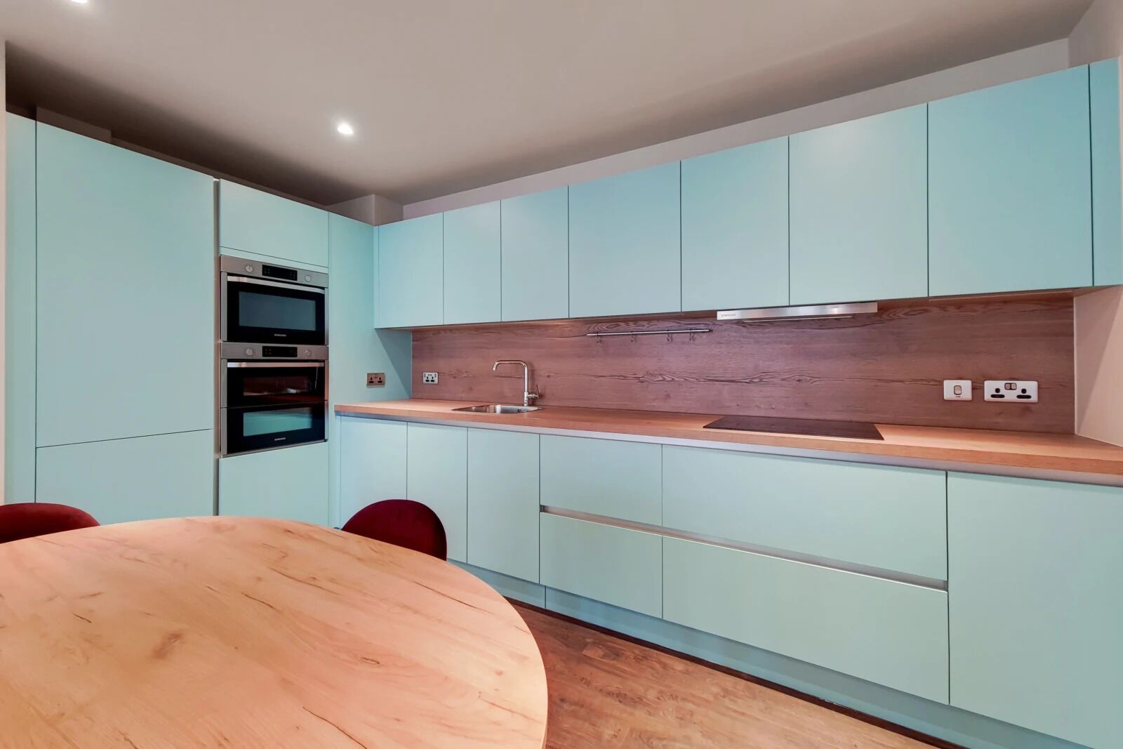 A modern kitchen with light blue cabinets, a wooden countertop, and built-in ovens.