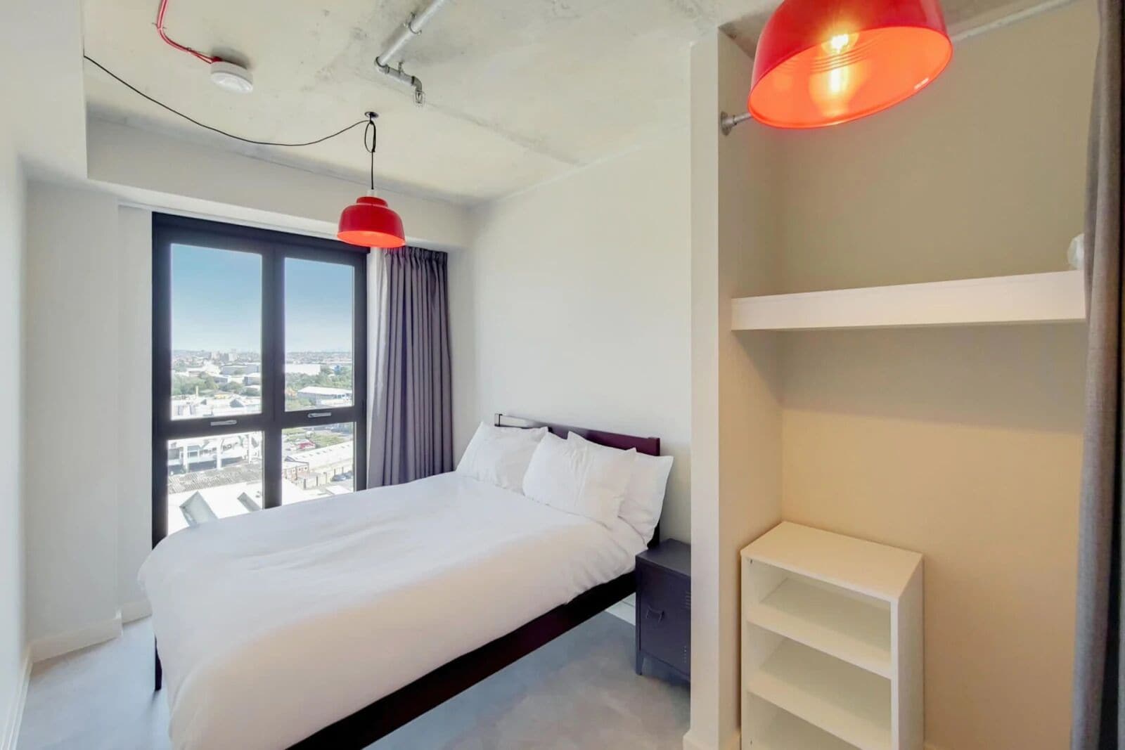 Una moderna camera d'hotel con un ampio letto, vista dalla finestra e una lampada a sospensione rossa.