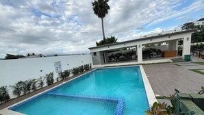 Une piscine rectangulaire dont les bords sont recouverts de carreaux, entourée d’un mur blanc et agrémentée d’un espace de repos abrité avec des bancs.