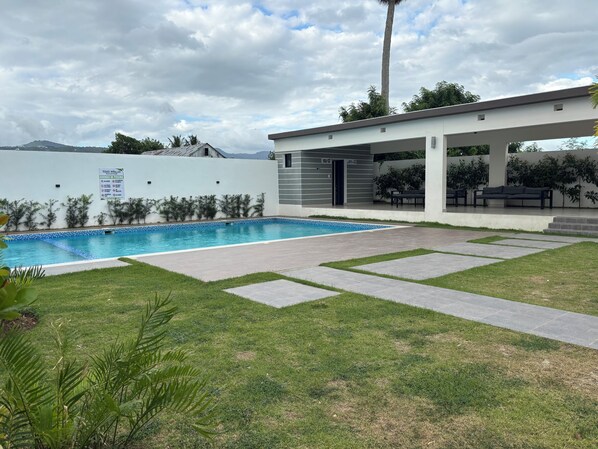A modern outdoor pool area with a covered seating area, a clear blue pool, and a grassy lawn. - Con piscina y cama king (Santiago de los Caballeros)