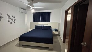 Une chambre à coucher avec un lit, une table de chevet, un ventilateur de plafond et une porte.