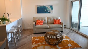 A modern living room with a sofa, orange cushions, a round wicker coffee table, and a large window. - New condo w/ fantastic view at west 17 Ave (Calgary)