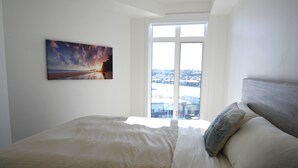 A bedroom with a large bed, a window with a view of a snowy landscape, and a painting on the wall. - New condo w/ fantastic view at west 17 Ave (Calgary)