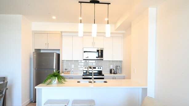 A modern kitchen with white cabinets, stainless steel appliances, and a central island with bar stools. - New condo w/ fantastic view at west 17 Ave (Calgary)