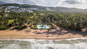A beach with a pool area, palm trees, and buildings in the background. - Rio Grande  Rio Mar cluster 2,Vista Del Mar- View (Río Grande)