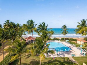 A resort with a swimming pool, palm trees, and a beach view. - Rio Grande Rio Mar cluster 2,Vista Del Mar- View (Río Grande)