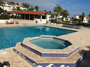 A swimming pool with a hot tub, surrounded by lounge chairs and palm trees.
