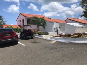 A parking lot with a red car and a golf cart. There are buildings with red-tiled roofs and white walls.