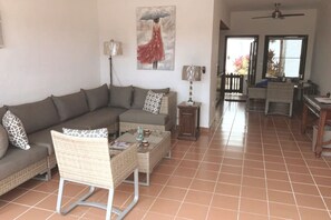 A living room with a sofa, a coffee table, and a chair. There is a painting on the wall and a lamp on a side table.