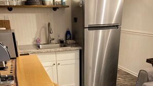 Una cocina con un refrigerador de acero inoxidable, una mesa de madera con dos taburetes amarillos y un sofá gris.