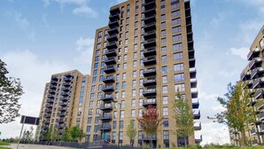A high-rise residential building with multiple balconies, a brick facade, and a clear sky.