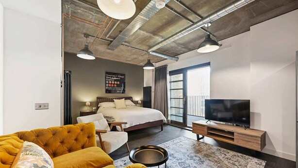 A modern hotel room with a large bed, a sofa, a TV, and a view of the city.