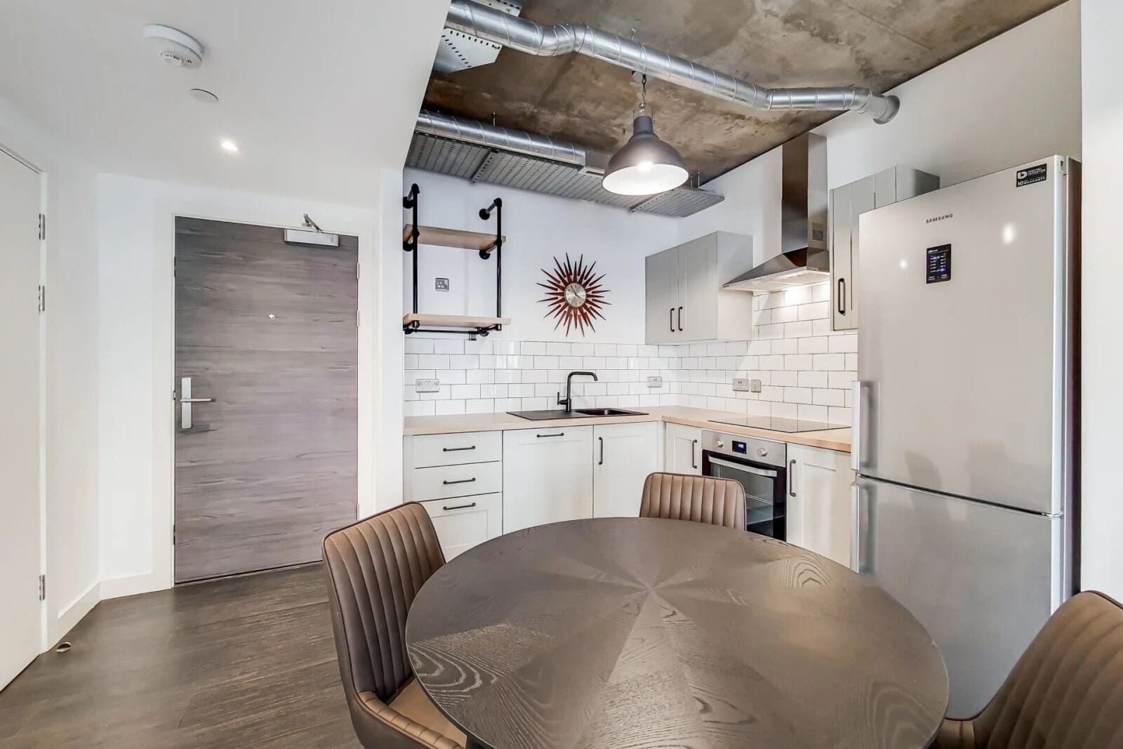 A modern kitchen with white cabinets, a stainless steel refrigerator, and a round dining table with chairs.