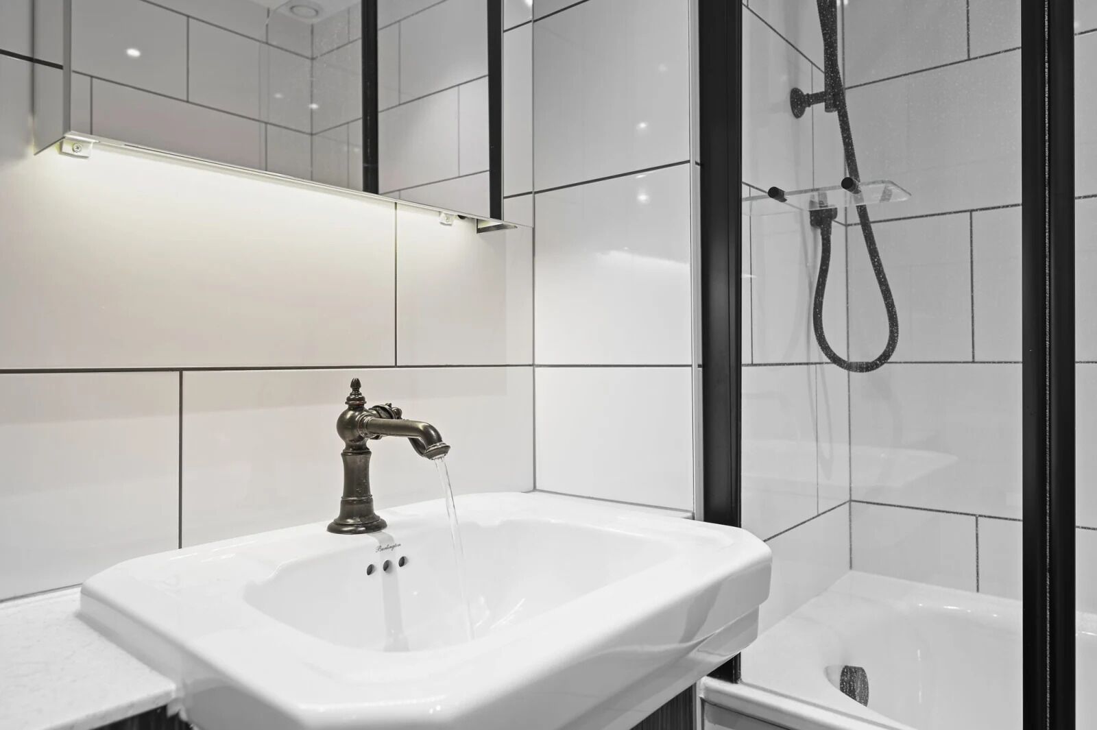 A modern bathroom with a white sink, a shower with a handheld showerhead, and a mirror above the sink.
