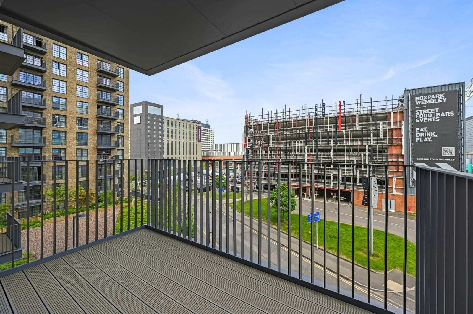 A balcony with a view of a cityscape, including a building under construction and a sign for Boxpark Wembley.