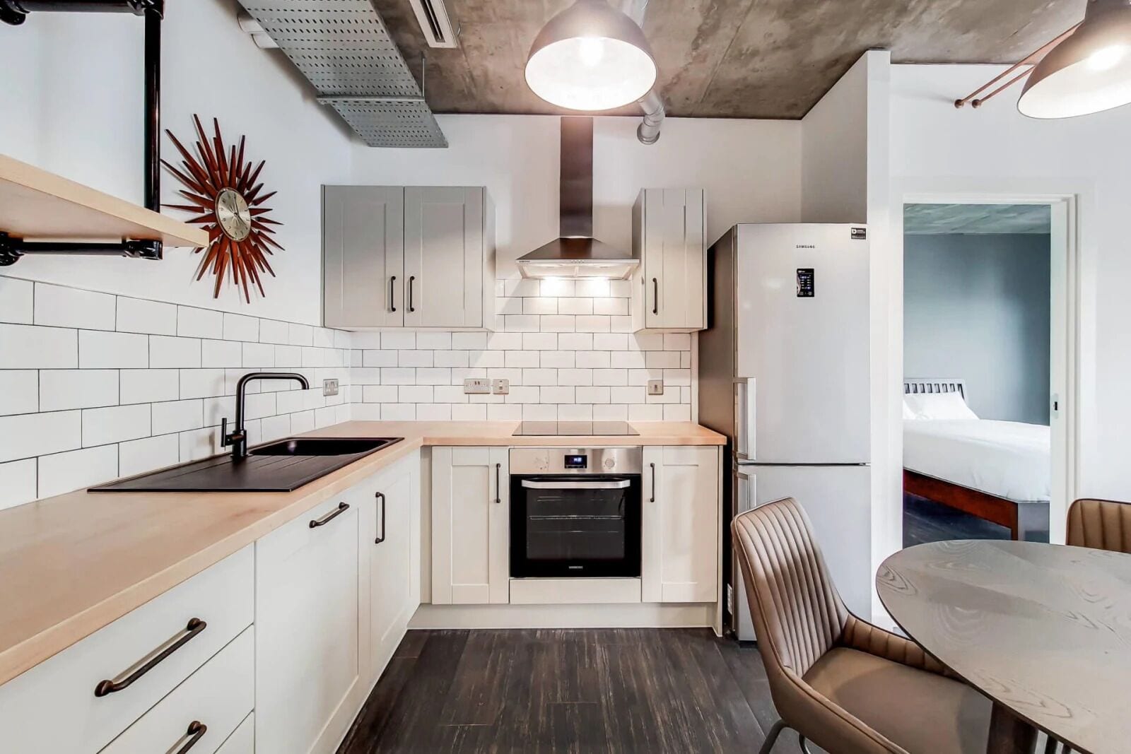 A compact kitchen with white cabinets, a built-in oven, and a refrigerator. There is a dining area with a table and chairs.