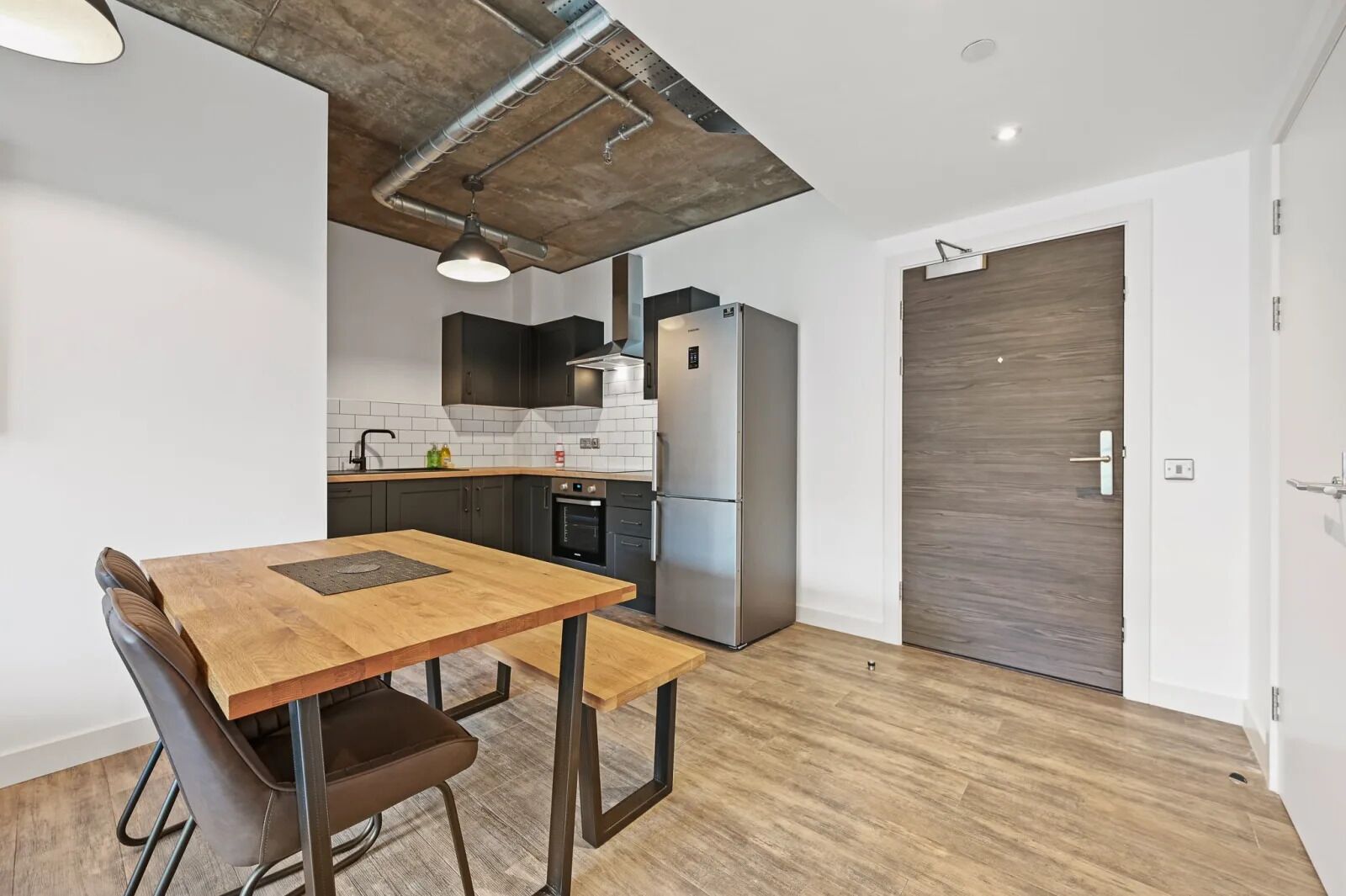 Une cuisine compacte avec une table et des chaises en bois, un four encastré et un réfrigérateur.
