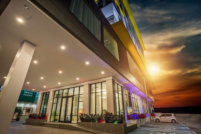 A modern hotel with a glass facade, a covered entrance, and a parking area.