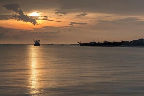 A calm body of water with a sunset in the background and a large ship in the distance. - Grand Flora Hotel (Melaka)
