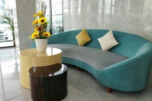 A teal sofa with two pillows, a vase with yellow flowers, and two round side tables. - Grand Flora Hotel (Melaka)