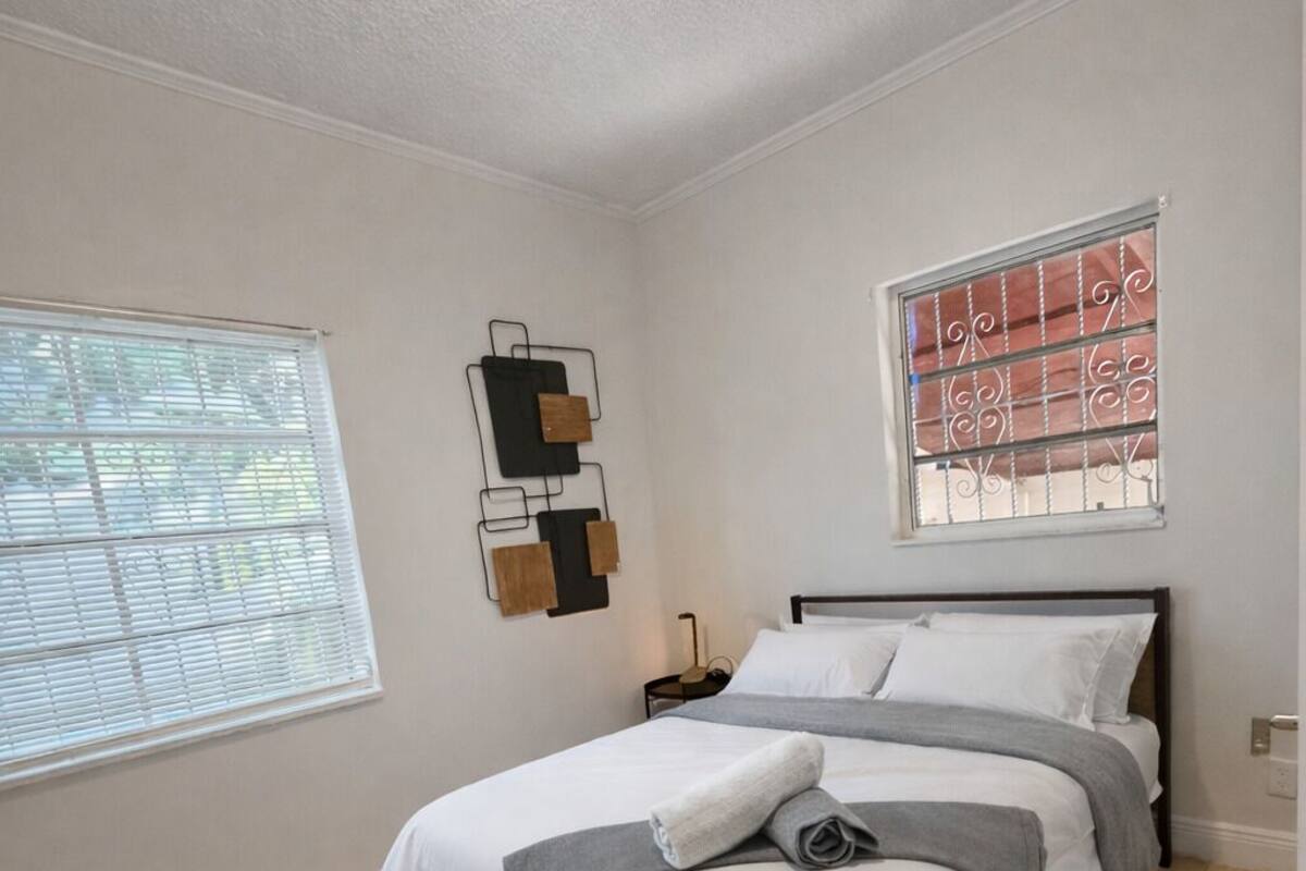A bedroom with a bed, a window with bars, a wall-mounted light fixture, and a ceiling light.