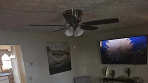 A living room with a ceiling fan, a flat-screen TV, two armchairs, a patterned rug, and a small table with decorative items. - Charming 2-bedroom condo with WiFi, AC in delightful Canton (Canton)