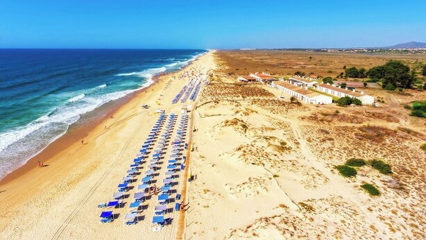 A beach with rows of blue umbrellas and white buildings in the background. - Freesia Villa, Santa Catarina da Fonte do Bispo, Tavira (Stº. Catarina Fonte do Bispo)