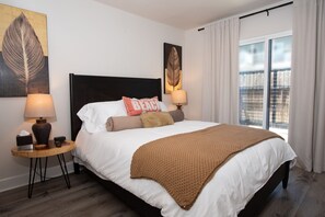Una cama bien hecha con una manta marrón, dos lámparas de noche y un cojín con la palabra 'BEACH'.