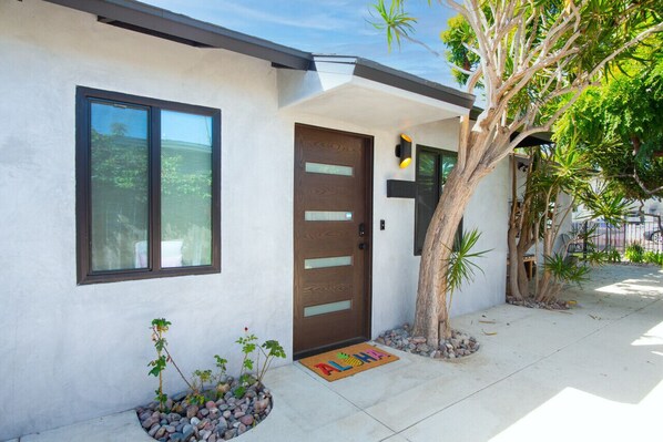 Una casa moderna con puerta marrón, ventanas amplias y un pequeño jardín con rocas y plantas.