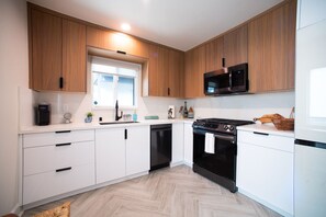 Eine moderne Küche mit Holzschränken, einem schwarzen Herd, einer Mikrowelle und einem Geschirrspüler.