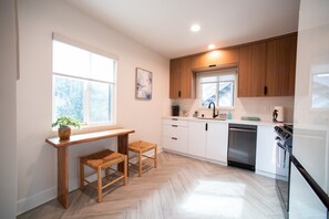 Una cocina moderna con armarios blancos, encimera de madera, horno empotrado y ventana que proporciona luz natural.