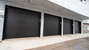 Fila de puertas de garaje cerradas, fachada de concreto y un letrero que indica una zona de estacionamiento.