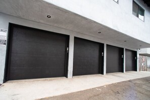A row of closed garage doors with a concrete facade and a sign indicating a parking area.