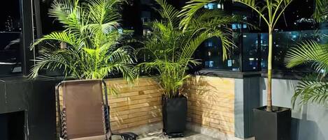 A rooftop terrace with a wooden ceiling, potted plants, and a foldable chair.
