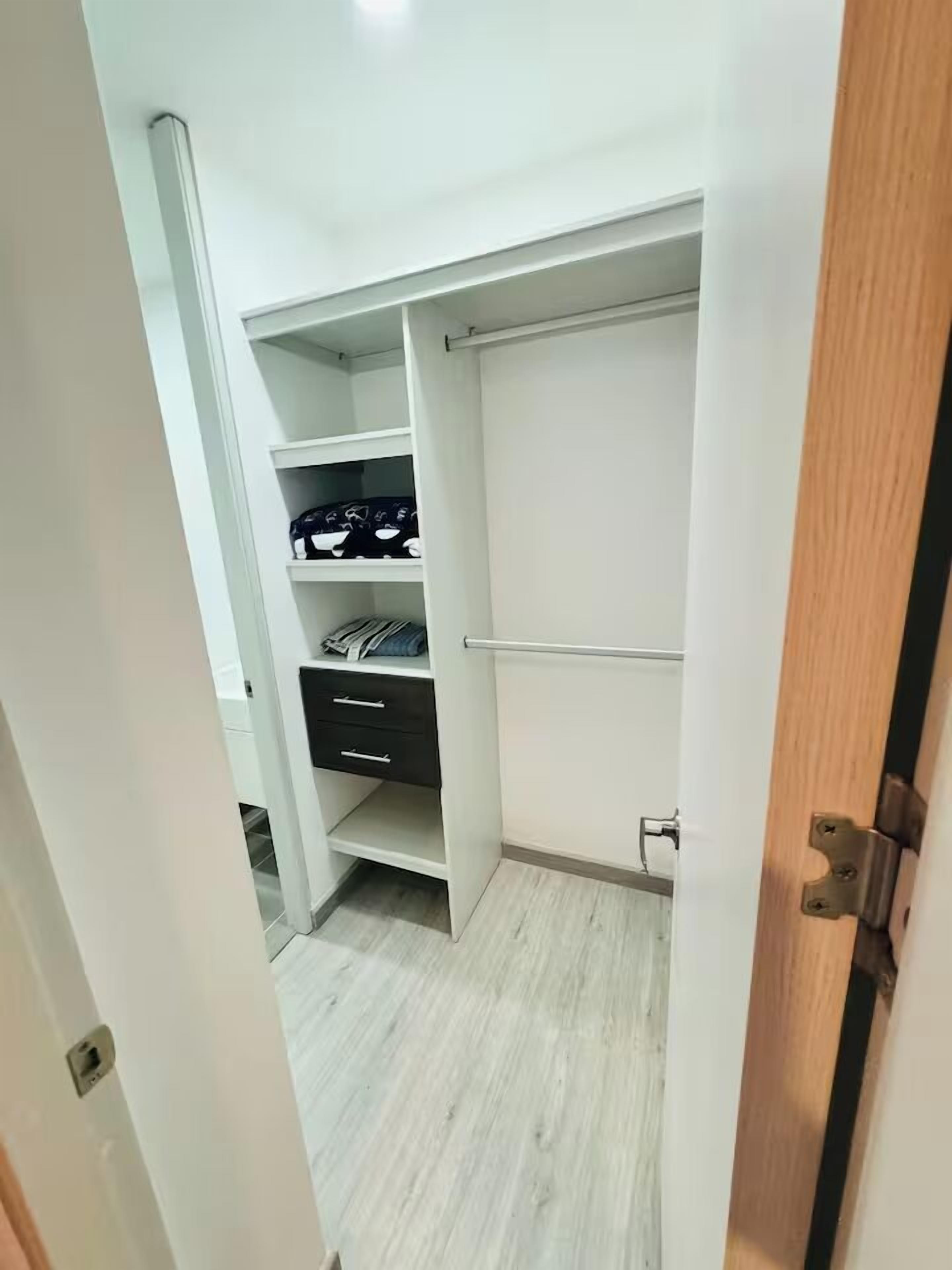 A walk-in closet with open shelves and drawers, a metal rod, and a wooden door.
