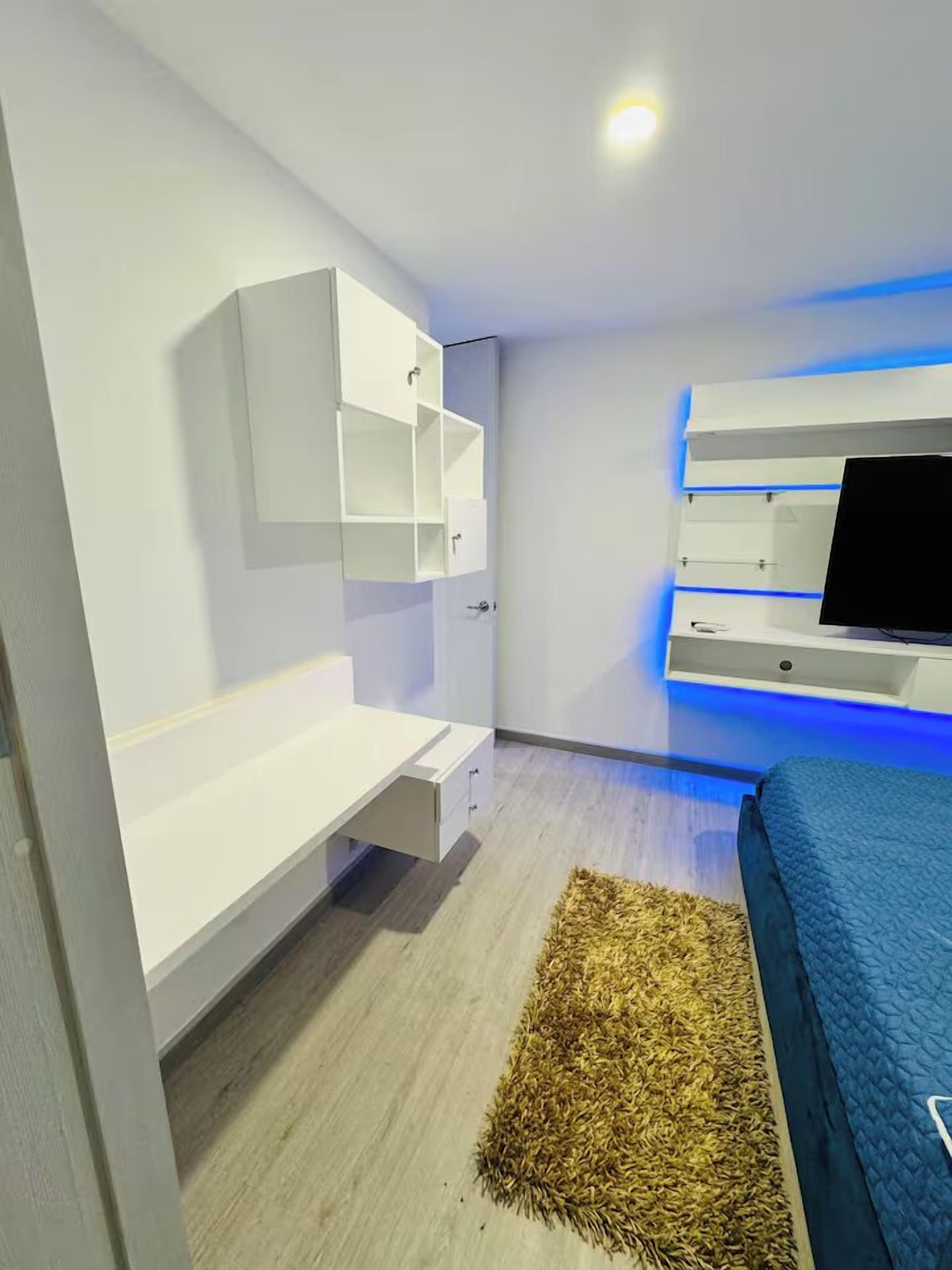 A modern bedroom with a bed, a desk, and a TV mounted on the wall.