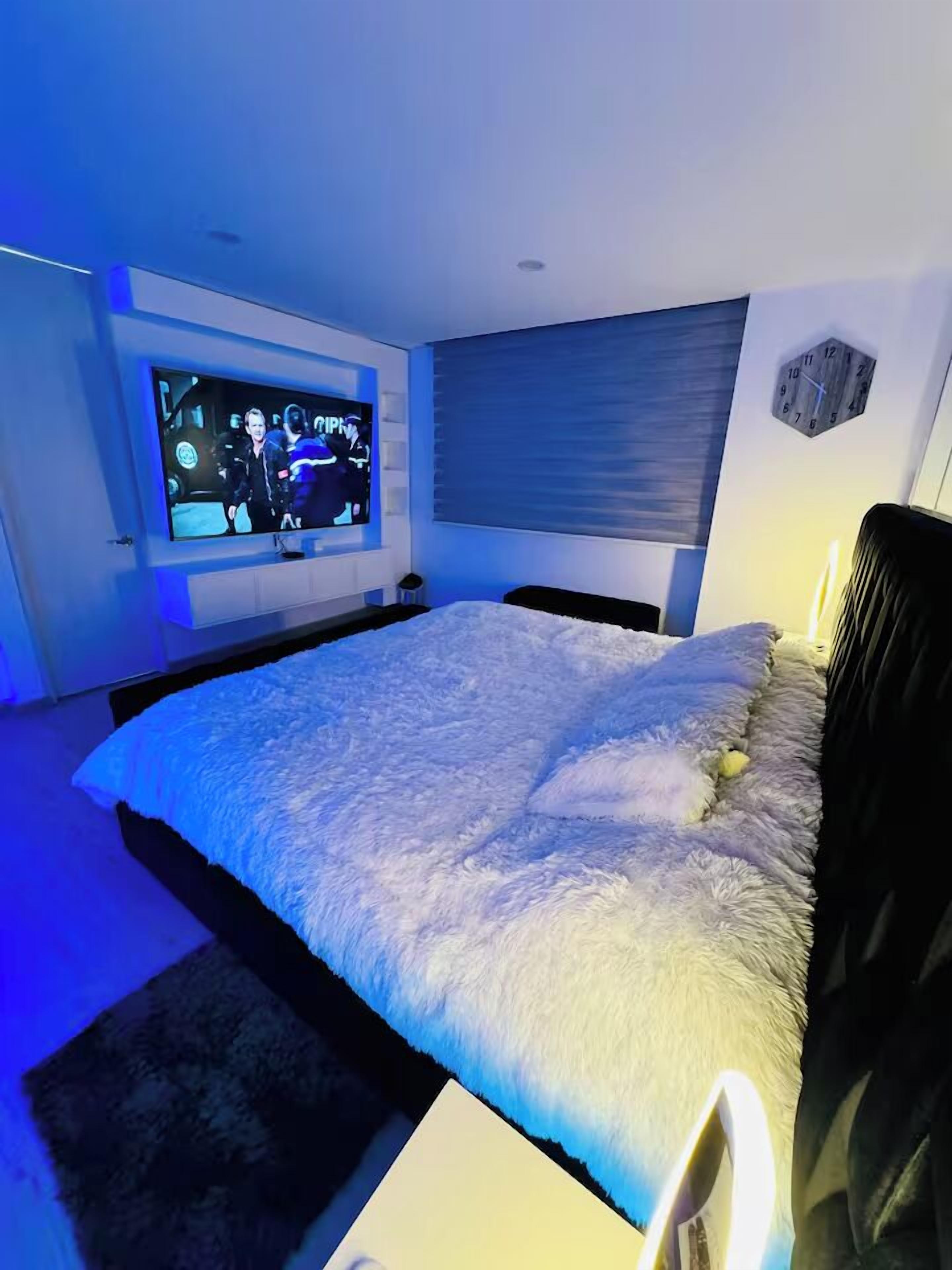 Un dormitorio moderno con una cama grande, un televisor de pantalla plana en la pared y una mesita de noche con lámpara.